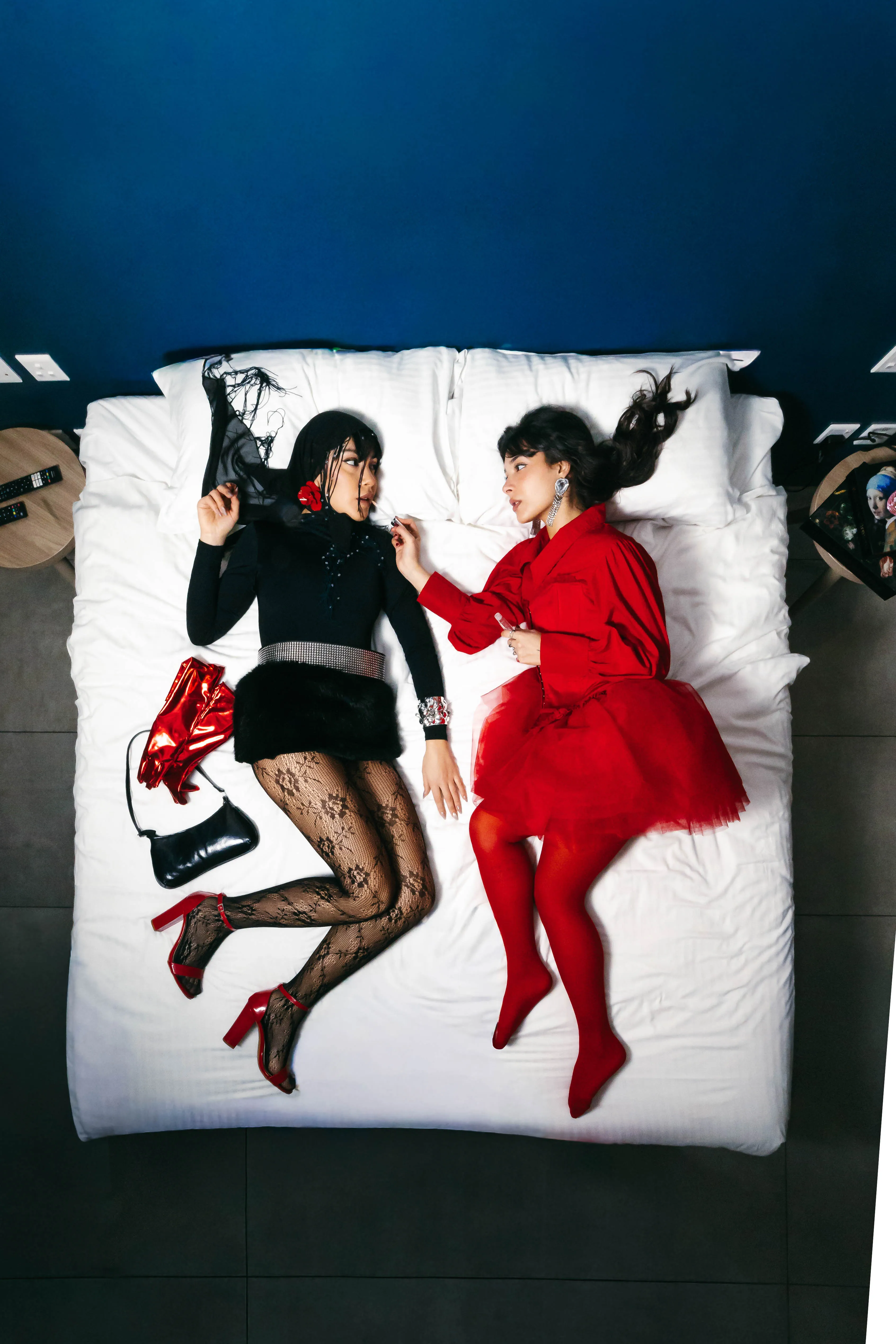 Two models in red and black lying on a white bed shot from above