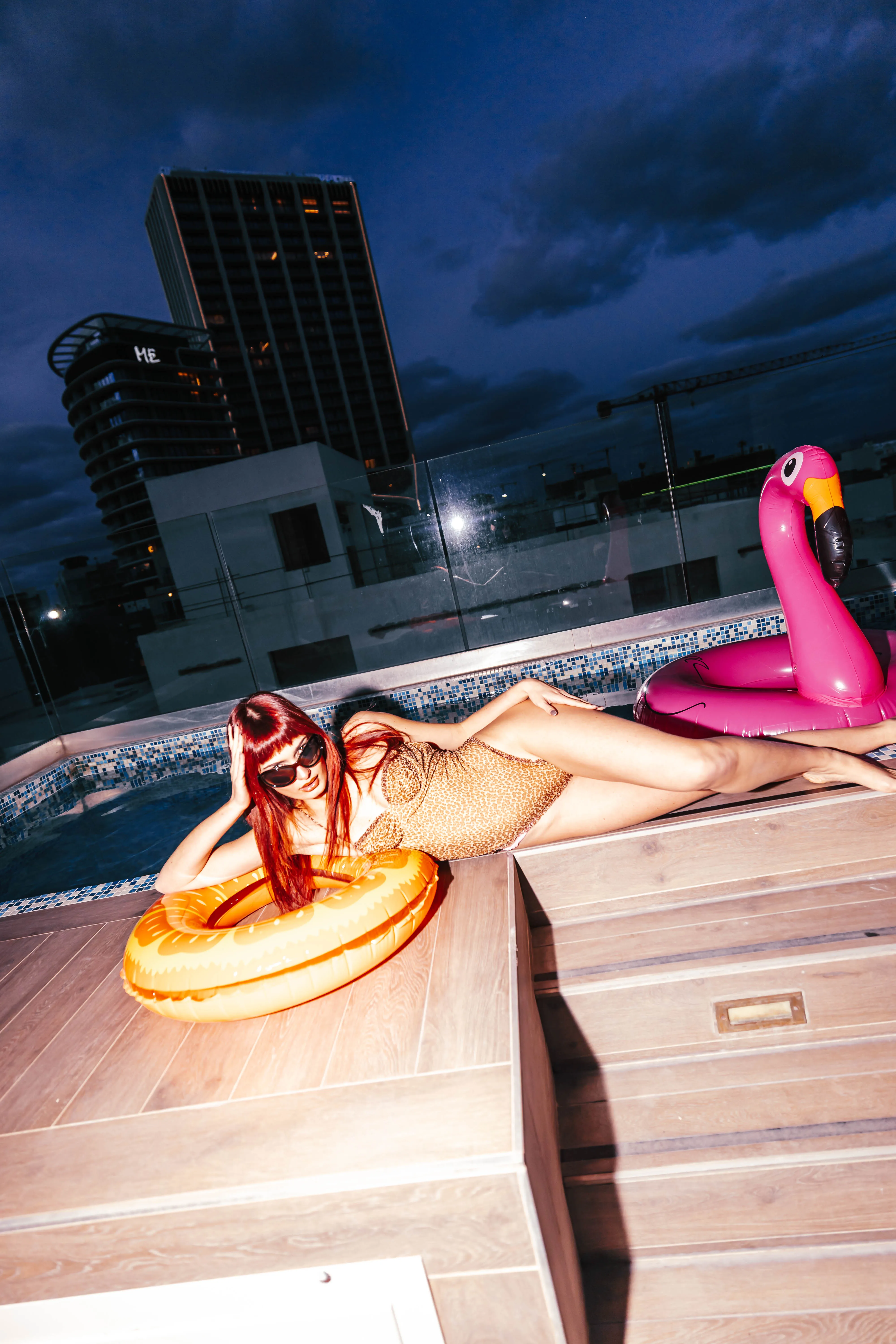Model lounging by the rooftop pool at dusk with flamingo float
