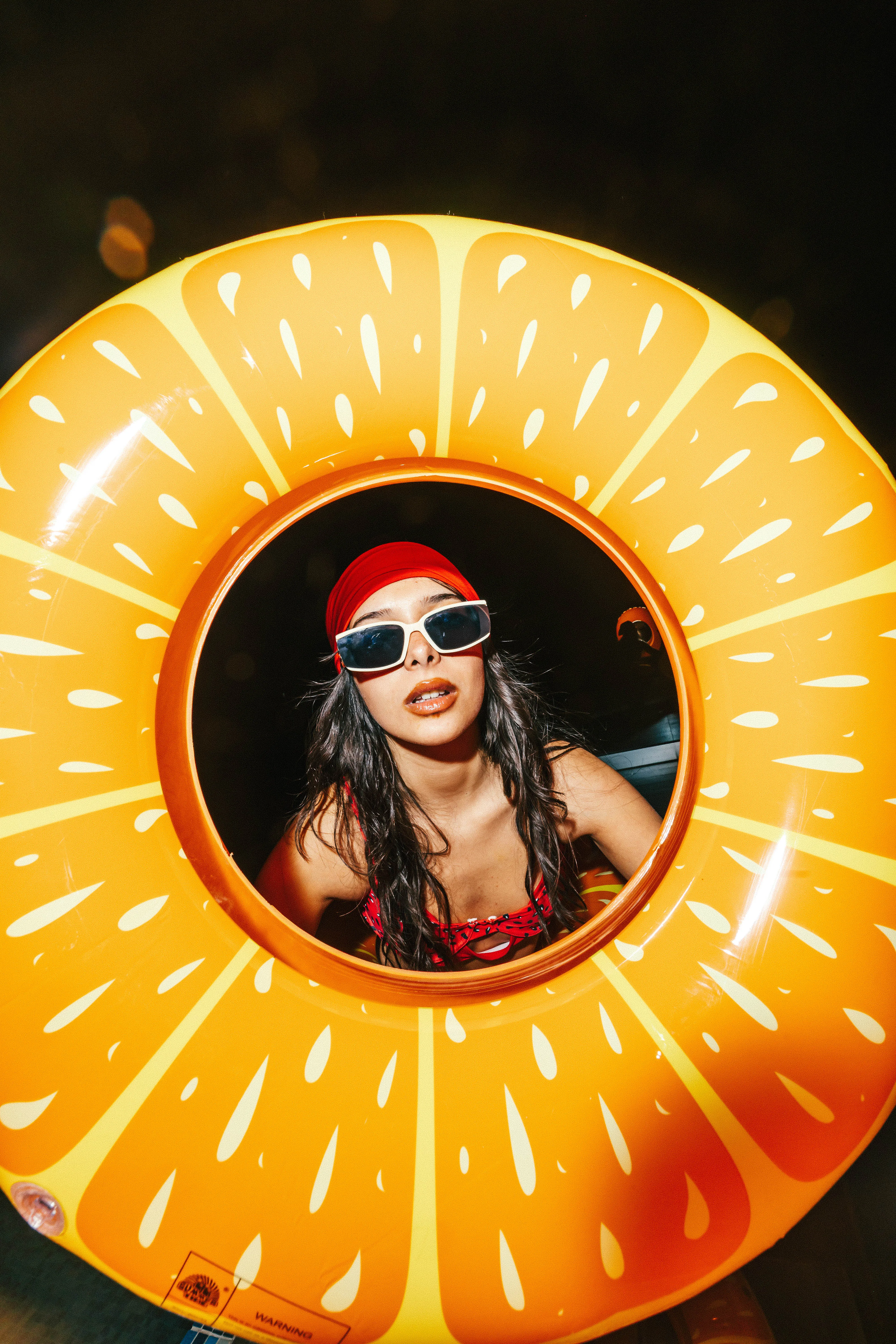 Model with sunglasses peering through an orange pool float